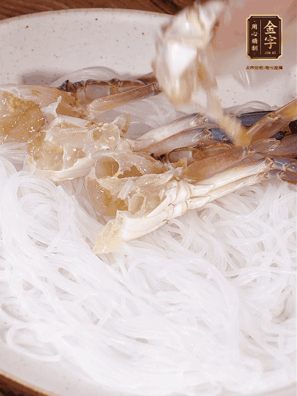 盤底墊上粉絲，擺上梭子蟹、火腿片，撒姜粒，淋上蒸魚豉油、花雕酒調(diào)味腌制15分鐘